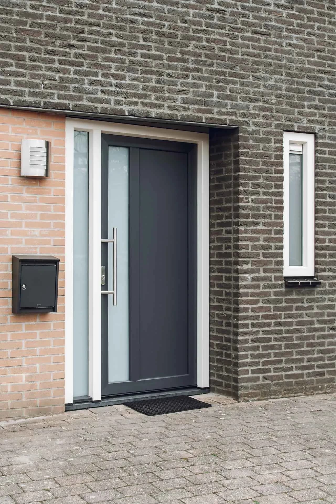 Antraciet voordeur met glazen zijlicht in een bakstenen gevel